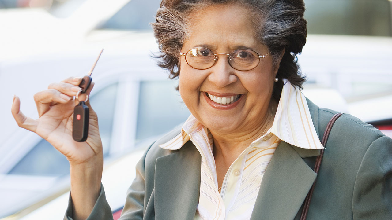 older woman with white-streaked hair smiling and holding up her car keys